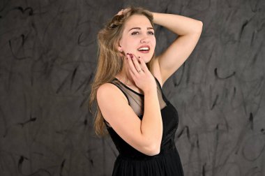 Siyah elbiseli, uzun saçlı ve mükemmel makyajlı güzel bir kızın fotoğrafı farklı pozlarda duruyor. Gri arka planda yatay kadın portresi evrensel kavramı.