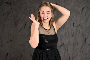 Siyah elbiseli, uzun saçlı ve mükemmel makyajlı güzel bir kızın fotoğrafı farklı pozlarda duruyor. Gri arka planda yatay kadın portresi evrensel kavramı.