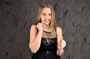 Siyah elbiseli, uzun saçlı ve mükemmel makyajlı güzel bir kızın fotoğrafı farklı pozlarda duruyor. Gri arka planda yatay kadın portresi evrensel kavramı.