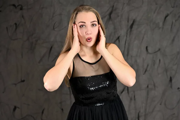 Uma foto de uma menina muito sorridente com cabelo comprido e excelente maquiagem em um vestido preto fica em poses diferentes. Conceito universal de retrato feminino horizontal sobre fundo alternativo cinza . — Fotografia de Stock