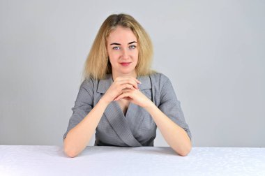 Model, kameranın tam karşısında çeşitli pozlarda oturuyor. Beyaz bir arka planda gri bir takım elbise içinde asgari makyajlı sevimli, gülümseyen sarışın bir iş kadını portresi..