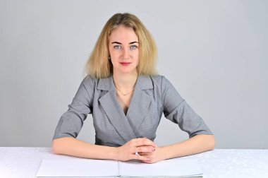 Model, kameranın tam karşısında çeşitli pozlarda oturuyor. Beyaz bir arka planda gri bir takım elbise içinde asgari makyajlı sevimli, gülümseyen sarışın bir iş kadını portresi..
