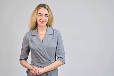 Çeşitli pozlarda kameranın önünde duran bir model. Beyaz bir arka planda gri bir takım elbise içinde asgari makyajlı sevimli, gülümseyen sarışın bir iş kadını portresi..