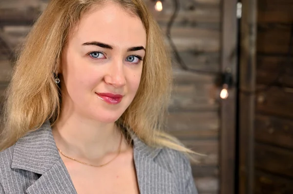 Ahşap bir arka planda iş elbisesi içinde asgari makyajlı güzel sarışın bir kadının yakın plan portresi. Kameranın karşısında çeşitli pozlarda duruyor..