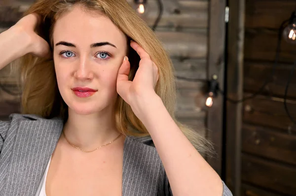 Retrato de cerca de una hermosa mujer rubia con un maquillaje mínimo en un traje de negocios sobre un fondo de madera. Se encuentra frente a la cámara en varias poses . — Foto de Stock