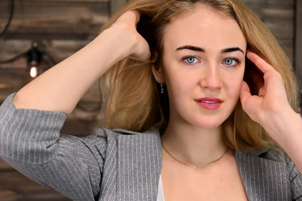 Retrato de cerca de una hermosa mujer rubia con un maquillaje mínimo en un traje de negocios sobre un fondo de madera. Se encuentra frente a la cámara en varias poses . — Foto de Stock