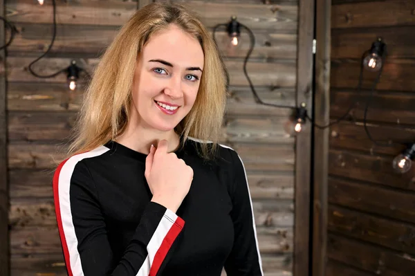 Ahşap bir arka planda eşofmanla asgari makyajlı güzel sarışın bir kadının yakın plan portresi. Kameranın karşısında çeşitli pozlarda duruyor..