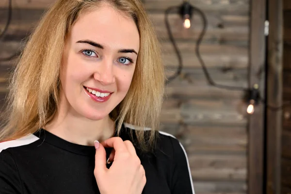 Ahşap bir arka planda eşofmanla asgari makyajlı güzel sarışın bir kadının yakın plan portresi. Kameranın karşısında çeşitli pozlarda duruyor..