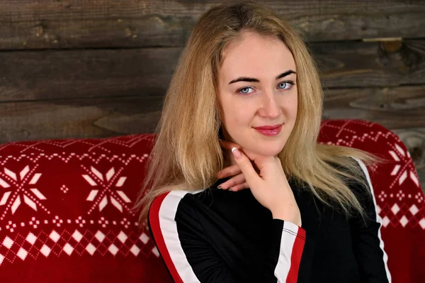 Porträtt av en ganska ung blond kvinna med minimal makeup i en sportklänning på en trä bakgrund. Sitter på en röd soffa mittemot kameran i olika poser. — Stockfoto