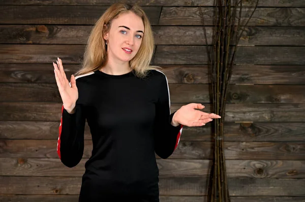 Porträt einer hübsch lächelnden jungen blonden Frau mit minimalem Make-up in einem schwarzen T-Shirt auf einem hölzernen Hintergrund. er steht der Kamera in verschiedenen Posen gegenüber. — Stockfoto