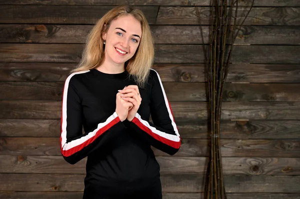 Güzel, gülümseyen sarışın bir kadının portresi. Asgari makyajlı, siyah tişörtlü, tahta arka planda. Kameranın karşısında çeşitli pozlarda duruyor..