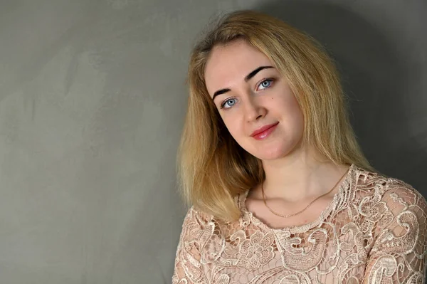 Porträtt av en ganska söt leende ung blond kvinna med minimal makeup i en beige blus på en grå bakgrund. Den står mittemot kameran i olika poser. — Stockfoto