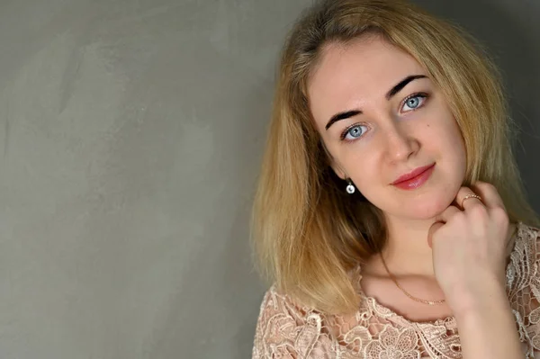 Porträtt av en ganska söt leende ung blond kvinna med minimal makeup i en beige blus på en grå bakgrund. Den står mittemot kameran i olika poser. — Stockfoto