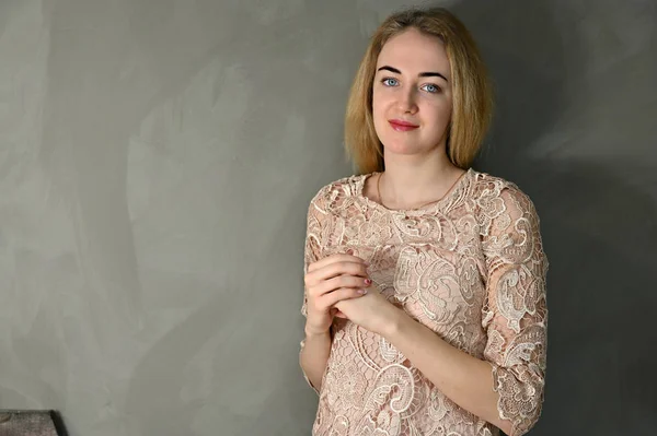 Porträtt av en ganska söt leende ung blond kvinna med minimal makeup i en beige blus på en grå bakgrund. Den står mittemot kameran i olika poser. — Stockfoto