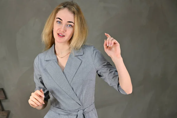 Retrato de una linda joven mujer de negocios rubia sonriente con un maquillaje mínimo en un traje gris sobre un fondo gris. Se encuentra justo enfrente de la cámara en varias poses . — Foto de Stock