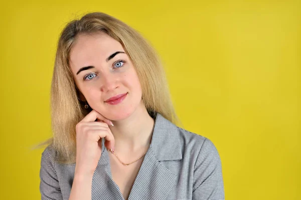 Närbild porträtt av en ganska söt leende ung blond affärskvinna med minimal makeup i en grå kostym på en gul bakgrund. Den står mittemot kameran i olika poser. — Stockfoto