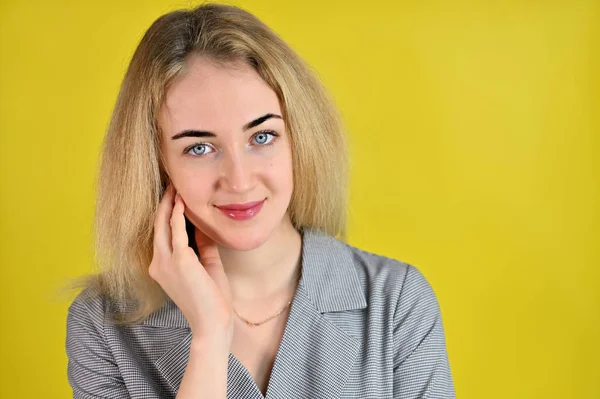 Ritratto ravvicinato di una giovane donna d'affari bionda piuttosto carina e sorridente con un trucco minimale in un abito grigio su uno sfondo giallo. Si trova direttamente di fronte alla fotocamera in varie pose . — Foto Stock