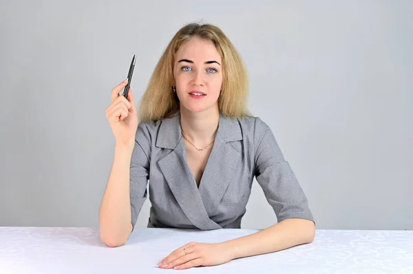 Retrato de uma linda e sorridente jovem mulher de negócios loira com maquiagem mínima em um terno cinza em um fundo branco. Modelo Senta-se em uma mesa diretamente em frente à câmera em várias poses . — Fotografia de Stock