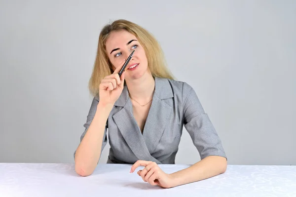 Portrait of a pretty cute smiling young blonde business woman with minimal makeup in a gray suit on a white background. Model Sits at a table directly opposite the camera in various poses. — 스톡 사진