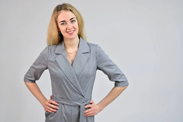 Modell, das in verschiedenen Posen direkt vor der Kamera steht. Porträt einer hübschen lächelnden jungen blonden Geschäftsfrau mit minimalem Make-up in einem grauen Anzug auf weißem Hintergrund. — Stockfoto