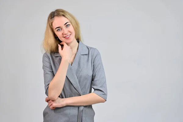 Modelo De pie directamente delante de la cámara en varias poses. Retrato de una linda joven mujer de negocios rubia sonriente con un maquillaje mínimo en un traje gris sobre un fondo blanco . — Foto de Stock