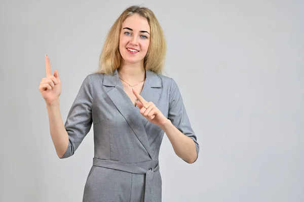 Retrato de una linda joven mujer de negocios rubia sonriente con un maquillaje mínimo en un traje gris sobre un fondo blanco. Modelo De pie directamente delante de la cámara en varias poses . — Foto de Stock