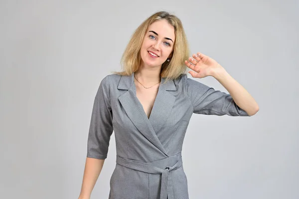 Portrait of a pretty cute smiling young blonde business woman with minimal makeup in a gray suit on a white background. Model Standing directly in front of the camera in various poses. — Stock Photo, Image