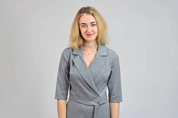 Portrait of a pretty cute smiling young blonde business woman with minimal makeup in a gray suit on a white background. Model Standing directly in front of the camera in various poses. — Stock Photo, Image