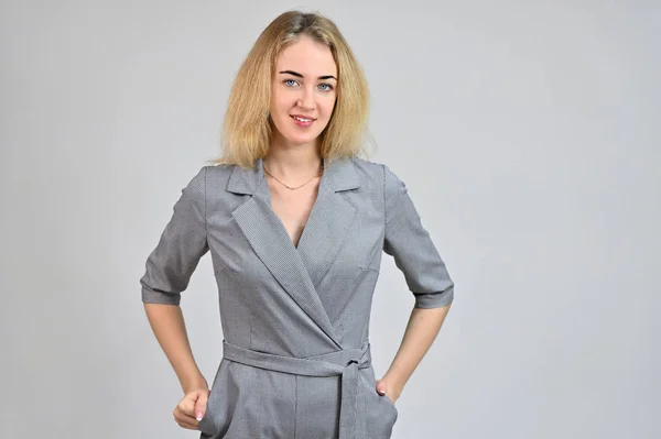 Portrait of a pretty cute smiling young blonde business woman with minimal makeup in a gray suit on a white background. Model Standing directly in front of the camera in various poses. — Stock Photo, Image