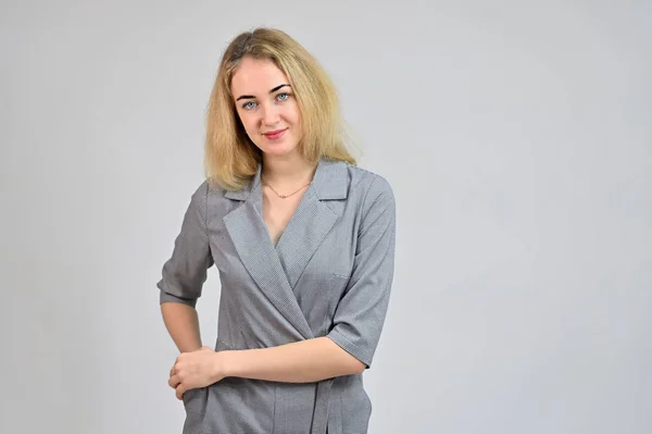 Portrait of a pretty cute smiling young blonde business woman with minimal makeup in a gray suit on a white background. Model Standing directly in front of the camera in various poses. — Stock Photo, Image