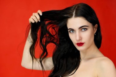 Uzun, güzel saç kavramı. Güzel esmer bir kızın yakın plan portresi mükemmel makyajlı ve lüks saçlı stüdyodaki kırmızı arka planda..