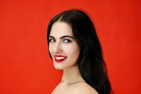 Das Konzept der hervorragenden Make-up und Kosmetik. Nahaufnahme Porträt eines hübschen brünetten Model-Mädchens mit hervorragendem Make-up und luxuriösen Haaren auf rotem Hintergrund im Studio. — Stockfoto