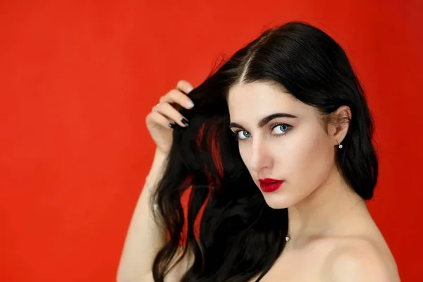 El concepto de cabello largo y hermoso. Close-up Retrato de una bonita modelo morena con excelente maquillaje y cabello lujoso sobre un fondo rojo en el estudio . — Foto de Stock