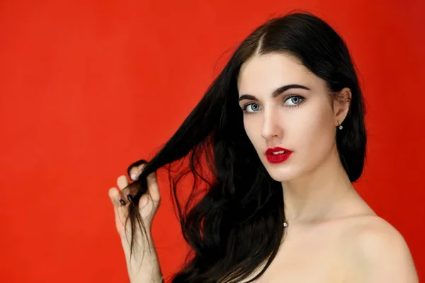 Das Konzept der langen schönen Haare. Nahaufnahme Porträt eines hübschen brünetten Model-Mädchens mit hervorragendem Make-up und luxuriösen Haaren auf rotem Hintergrund im Studio. — Stockfoto