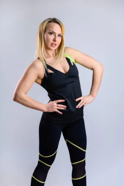 Full-length vertical photo of a pretty slender blonde woman athlete in a sports suit on a white background. The concept of effective fitness. Standing in different poses with emotions and a smile. — 스톡 사진