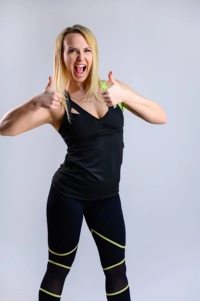 Foto vertical de cuerpo entero de una atleta rubia bastante delgada con un traje deportivo sobre un fondo blanco. El concepto de aptitud efectiva. De pie en diferentes poses con emociones y una sonrisa . — Foto de Stock