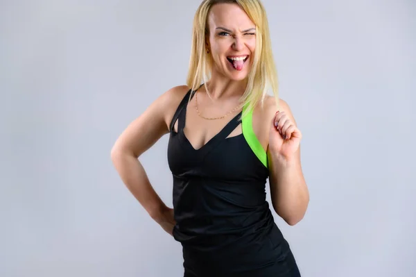 Foto de uma mulher loira muito magra atleta em um traje de treino em um fundo branco. O conceito de aptidão eficaz. De pé em diferentes poses com emoções e um sorriso . — Fotografia de Stock