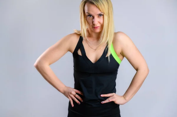 Foto van een vrij slanke blonde vrouw atleet in een trainingspak op een witte achtergrond. Het concept van effectieve fitness. In verschillende houdingen staan met emoties en een glimlach. — Stockfoto