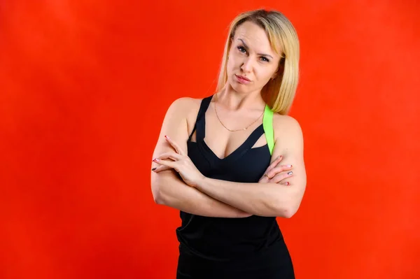 Foto de uma bela mulher muito magra esportista loira em um traje de treino em um fundo vermelho. O conceito de aptidão na moda. De pé em diferentes poses com emoções e um sorriso . — Fotografia de Stock