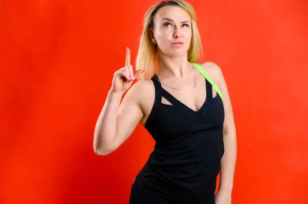 Foto di una bella donna piuttosto magra sportiva bionda in tuta su uno sfondo rosso. Il concetto di fitness alla moda. In diverse pose con emozioni e un sorriso . — Foto Stock