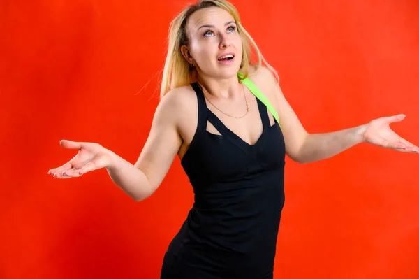 The concept of fashionable fitness. Photo of a beautiful pretty slim woman blonde sportswoman in a tracksuit on a red background. Standing in different poses with emotions and a smile. — 스톡 사진