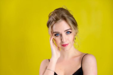 Glamorous beauty front view portrait of a pretty blonde model with excellent make-up and beautiful hairstyle on a yellow background in the studio. The concept of cosmetics, fashion and style.