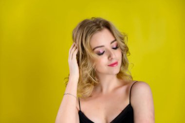 Glamorous beauty front view portrait of a pretty model with blond hair with great makeup and a beautiful hairstyle on a yellow background in the studio. The concept of cosmetics, fashion and style.
