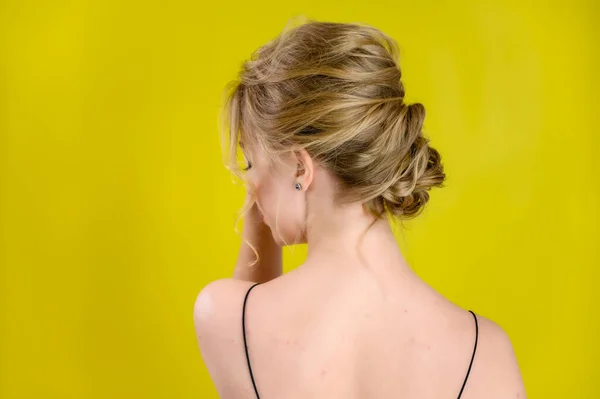 Glamorous beauty rear view portrait of a pretty blonde model with excellent make-up and beautiful hairstyle on a yellow background in the studio. The concept of cosmetics, fashion and style. — Stock Photo, Image