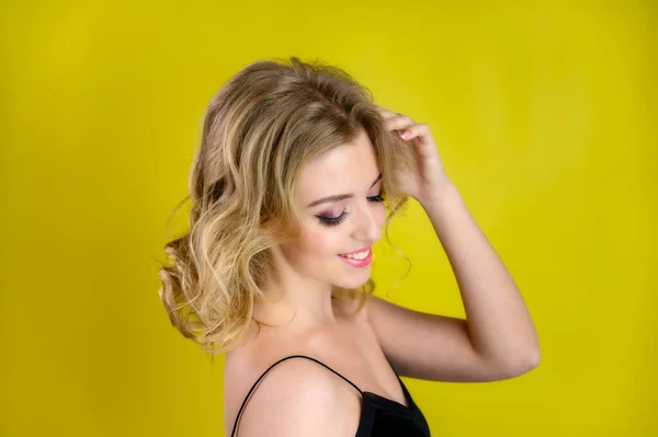 Portrait de beauté glamour vue de côté d'un joli modèle aux cheveux blonds avec un excellent maquillage et une belle coiffure sur un fond jaune en studio. Le concept de cosmétique, de mode et de style . — Photo