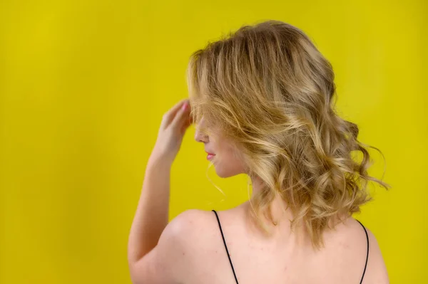 Beauté glamour vue arrière portrait d'un joli modèle aux cheveux blonds avec un grand maquillage et une belle coiffure sur un fond jaune dans le studio. Le concept de cosmétique, de mode et de style . — Photo