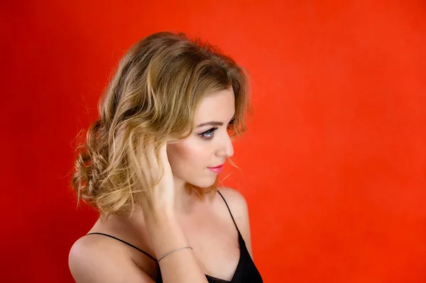 Glamorös skönhet porträtt sida bild av en vacker modell med blont hår med stor makeup och en vacker frisyr på en röd bakgrund i studion. Begreppet kosmetika, mode och stil. — Stockfoto