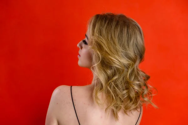 Bellezza glamour vista posteriore ritratto di un grazioso modello con i capelli biondi con grande trucco e una bella acconciatura su uno sfondo rosso in studio. Il concetto di cosmetici, moda e stile . — Foto Stock