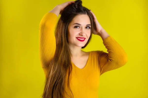 Πορτρέτο ενός όμορφου μελαχρινού κοριτσιού με μακριά μαλλιά με χαμόγελο σε κίτρινο πουλόβερ σε κίτρινο φόντο χαμογελά και δείχνει θετικά συναισθήματα — Φωτογραφία Αρχείου