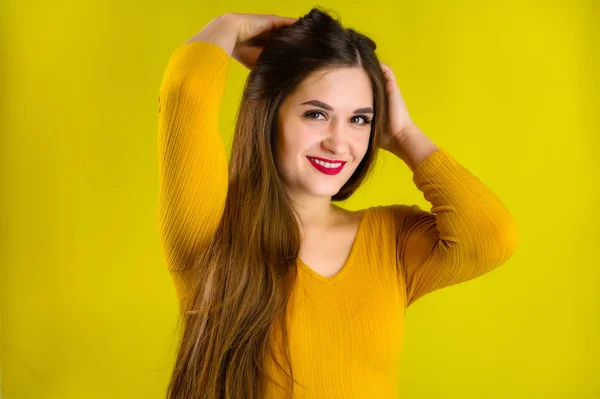 노란 배경에 노란 스웨터를 입은 예쁜 갈색 머리의 소녀가 노란 배경에 미소를 짓고 긍정적 인 감정을 보이는 모습 — 스톡 사진